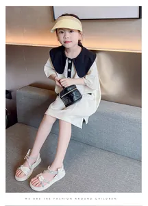 Full view of a young girl wearing stylish white rhinestone bow sandals on a grey sofa.