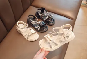 Close-up of beige girls' sandals with rhinestones and bows on a soft leather background