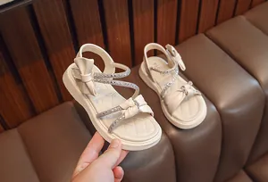 Detail view of elegant girls' cream sandals with rhinestone straps and decorative bow