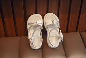Detail view showing cream girl's sandals with rhinestone straps and elegant side bow