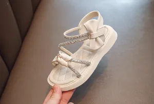 Detailed view of cream girls' sandals with sparkling rhinestones and a elegant bow knot.
