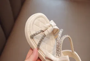 Close-up detail of girls' rhinestone bow sandals with quilted cream leather insoles