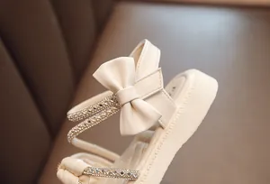 Detail shot of elegant cream girl's sandal featuring bow and rhinestone straps