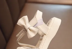 Detailed macro view showing sparkling rhinestones and a soft cream bow on a girls' sandal