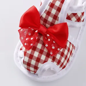 Close-up of baby sandal with red gingham pattern and large decorative bow detail.