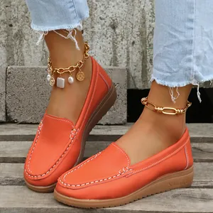 Gros plan de mocassins pour femmes orange vif avec coutures contrastées sur bois.