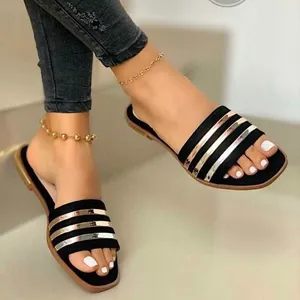 Vue rapprochée d'élégantes sandales plates noires avec brides métalliques dorées