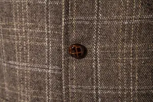 Détail de près du tissu en tweed à carreaux marron et d'un bouton tressé sur un gilet pour homme