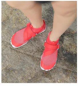Red breathable mesh water shoes with velcro strap on natural rocky beach terrain