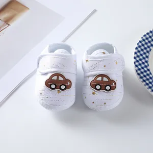 Close-up view of white infant soft sole canvas shoes with cute brown car applique details