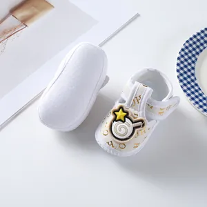 Close-up of white baby cloth shoes with gold OH pattern and soft anti-slip sole