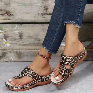 Macro detail of women's leopard print wedge flip-flop sandals worn with blue denim jeans