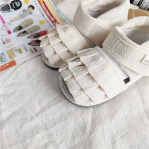 Detailansicht von cremefarbenen Kleinkindsandalen für Mädchen mit Rüschen und weicher Sohle.