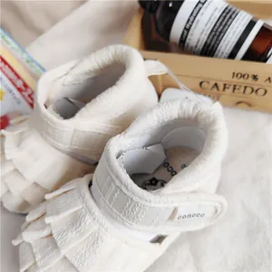 Detailansicht der cremefarbenen Baby-Mädchen-Sandalen mit Fransen und conoco-Logo