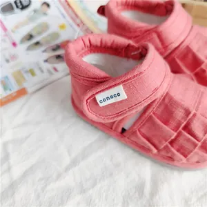 Nahaufnahme einer rosa gewebten Kleinkindersandale mit conoco-Markenetikett am Riemen
