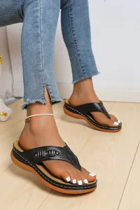 Primo piano di infradito con zeppa nera da donna con decorazioni metalliche eleganti