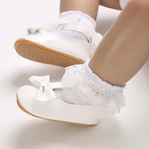 Nahaufnahme von weißen Baby-Lauflernschuhen mit Schleife und Spitzen-Rüschensocken.