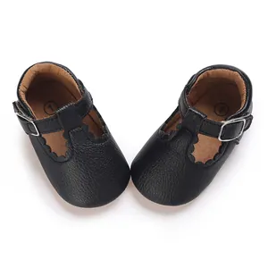 Close-up of black faux leather baby shoes with scalloped edges and T-strap buckle
