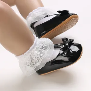 Nahaufnahme von schwarzen Lackleder-Babyschuhen mit Schleife und weißen Spitzen-Söckchen