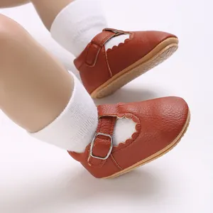 Macro view of brown faux leather baby Mary Janes with scalloped edges and buckle straps.