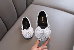 Nahaufnahme silberner Glitzerschuh für Mädchen mit großer weißer Schleife und Perlen