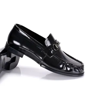 Primer plano de mocasines clásicos de hombre en charol negro con detalle de bocado metálico.