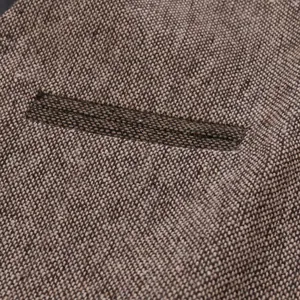 Gros plan sur la texture du tissu tissé et le détail de la poche d'un gilet en tweed marron.