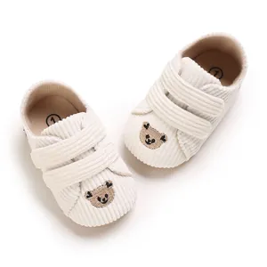 Détail de chaussures bébé en velours côtelé crème avec broderie ours et scratchs.