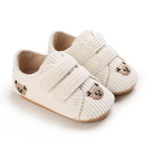 Gros plan de baskets bébé en velours côtelé blanc cassé avec broderie ours et velcro