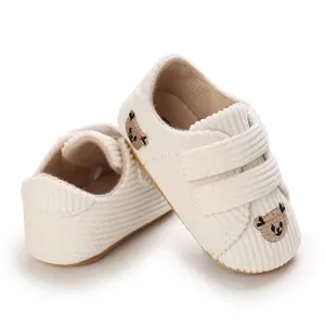 Détail de chaussures bébé en velours côtelé blanc avec broderie ours et attaches velcro souples