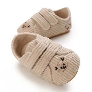 Détail de chaussures pour bébé en velours côtelé beige avec ours brodé et lanières