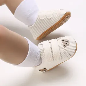 Détail de chaussures bébé en velours côtelé blanc avec broderie ours et scratch.