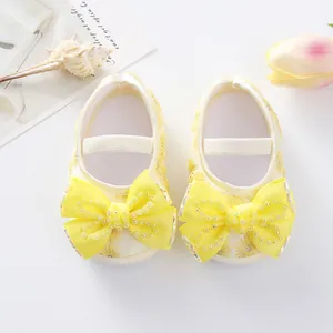 Close-up detail of cute yellow baby princess shoes with large ribbon bows and beads.