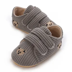 Gros plan de chaussures bébé en velours côtelé gris avec broderie ours.