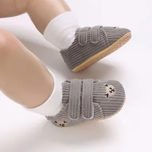 Gros plan de chaussures bébé en velours côtelé gris avec broderie ours et scratchs