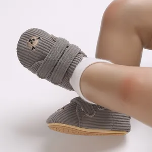 Gros plan de chaussures bébé en velours côtelé gris avec broderie animalière et semelle souple.
