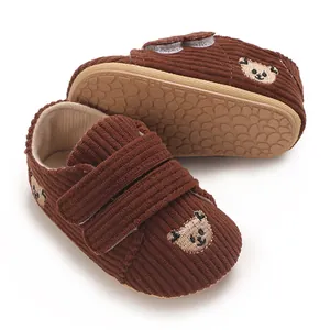 Détail de chaussures bébé en velours marron avec broderie ours et semelle antidérapante.