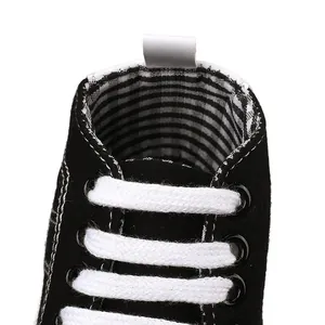 Gedetailleerde close-up van zwarte canvas baby-stapschoenen met witte veters en strepen