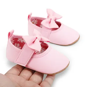 Primer plano de zapatos de princesa rosas para bebé con lazo grande sostenidos en la mano