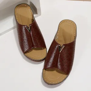 Detailansicht brauner Bohemian-Wedge-Slipper mit Lochmuster und goldenem V-Metalldekor.
