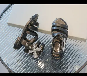 Detalle de sandalias romanas negras para niños con una mariposa de pedrería brillante