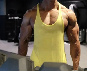 Close-up of a muscular man wearing a yellow cotton racerback fitness tank top in a gym.