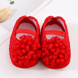 Détail de chaussures de princesse rouges pour nouveau-né avec grande fleur décorative.