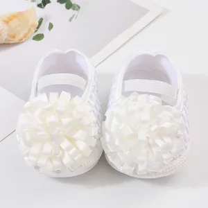 Gros plan de chaussures de princesse pour bébé blanches avec de grandes fleurs en ruban.