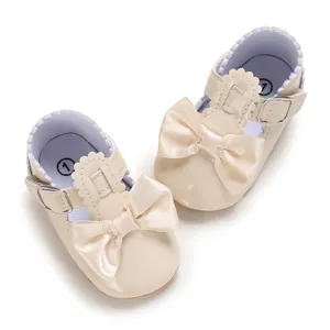 Dettaglio di scarpine da neonata in vernice beige con grandi ed eleganti fiocchi di raso