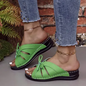 Primer plano de sandalias de cuña verdes con detalle de lazo en los pies de la modelo