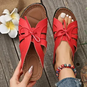 Primer plano de sandalias rojas con cuña y lazo sobre fondo de madera rústica.