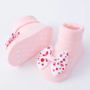Primer plano de calcetines rosa para bebé con lazo de lunares rojos y suela antideslizante.