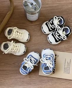 Detailed top view of baby canvas sneakers in cream, black, and blue denim on wood.