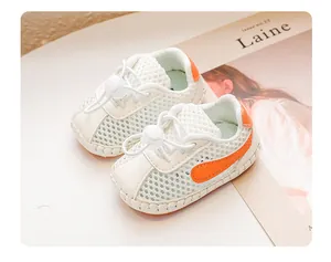 Nahaufnahme weißer atmungsaktiver Mesh-Babysandalen mit orangefarbenen Akzenten.